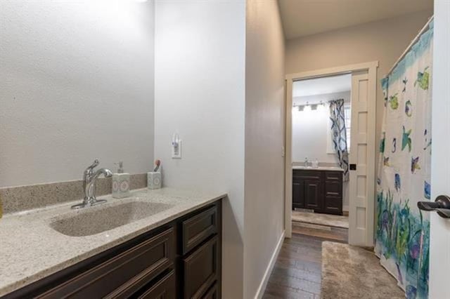 bathroom with two vanities, wood finished floors, baseboards, and a sink