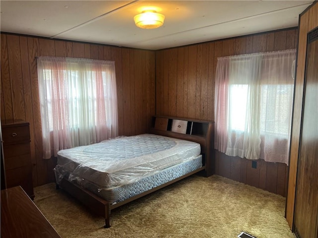 bedroom featuring carpet flooring, wooden walls, and multiple windows