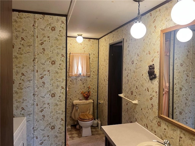 bathroom with toilet, wallpapered walls, vanity, and ornamental molding