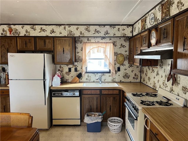 kitchen featuring a sink, white appliances, dark brown cabinetry, wallpapered walls, and light floors