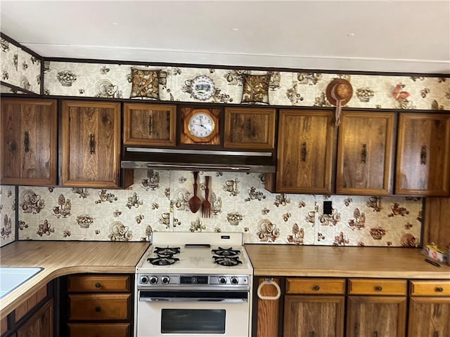 kitchen featuring under cabinet range hood, gas range gas stove, and wallpapered walls