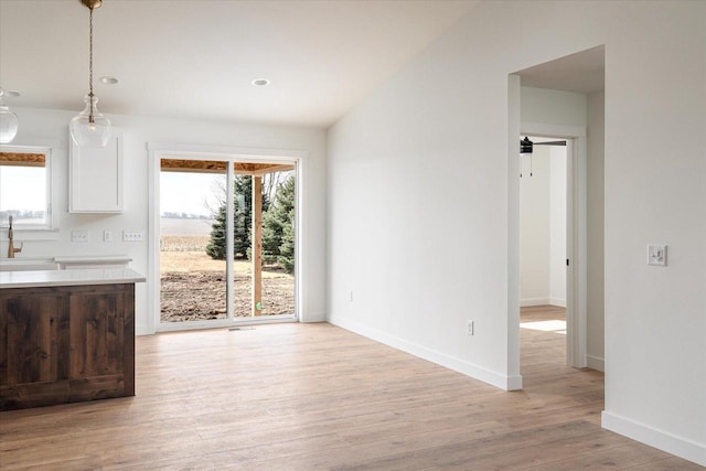 unfurnished dining area featuring vaulted ceiling, baseboards, light wood-type flooring, and a sink