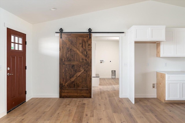 entryway with vaulted ceiling, a barn door, baseboards, and light wood finished floors