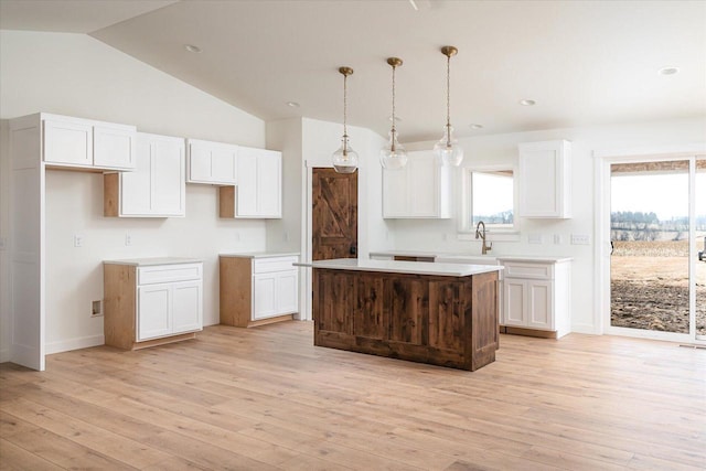 kitchen with light wood finished floors, a kitchen island, decorative light fixtures, white cabinets, and a sink