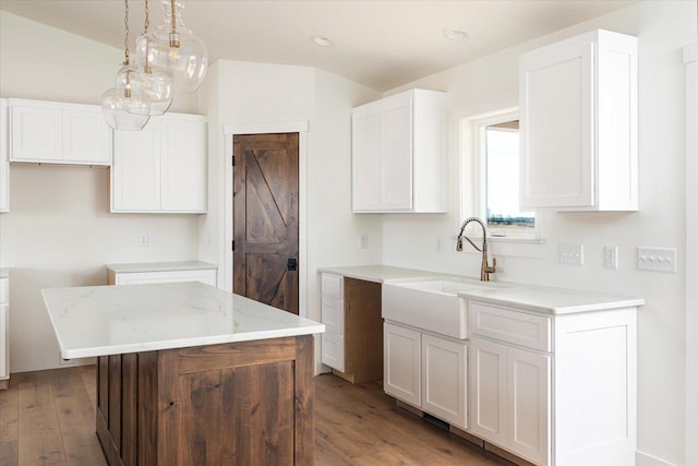 kitchen with light wood finished floors, a kitchen island, light stone counters, white cabinets, and a sink