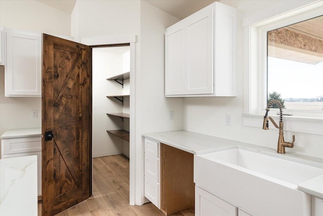 interior space with light stone counters, white cabinetry, light wood-type flooring, and a sink