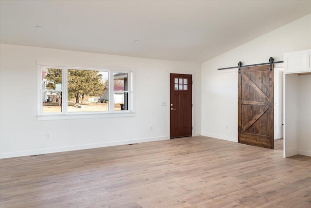 entryway featuring visible vents, baseboards, lofted ceiling, a barn door, and light wood-style flooring