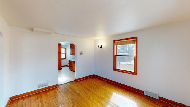 spare room with baseboards, visible vents, arched walkways, and light wood-type flooring