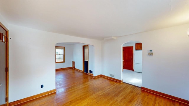 spare room featuring arched walkways, light wood-type flooring, and baseboards