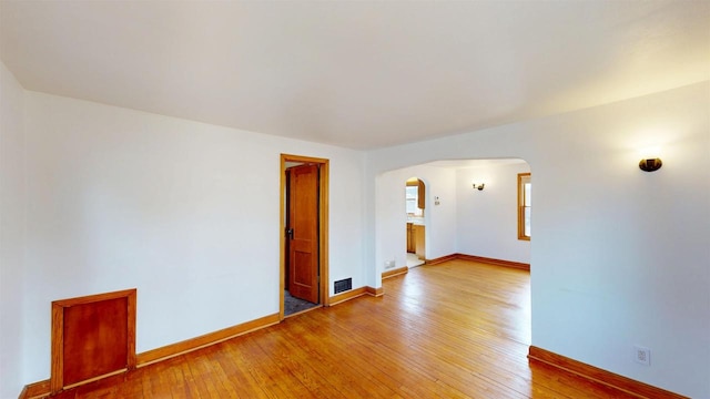 unfurnished room with visible vents, arched walkways, baseboards, and light wood finished floors