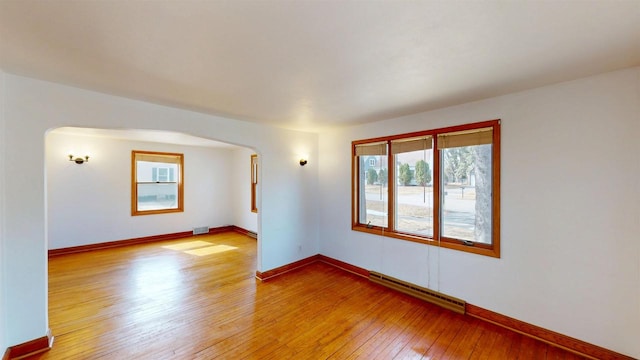 spare room with visible vents, light wood-style flooring, arched walkways, a baseboard radiator, and baseboards