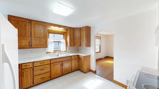 kitchen with light floors, light countertops, freestanding refrigerator, arched walkways, and a sink