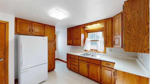 kitchen featuring a sink, freestanding refrigerator, brown cabinetry, light countertops, and light floors