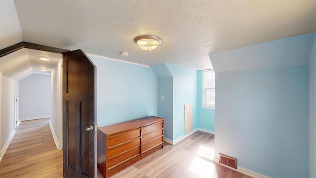 additional living space with visible vents, light wood-style flooring, a textured ceiling, and baseboards