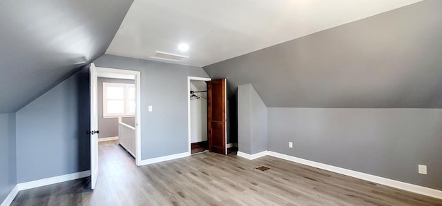 additional living space featuring visible vents, light wood-style flooring, baseboards, and vaulted ceiling