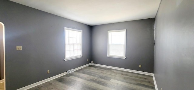 spare room featuring arched walkways, baseboards, and wood finished floors