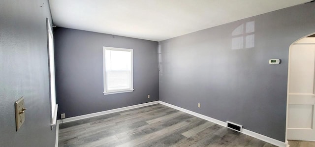 unfurnished room featuring visible vents, arched walkways, baseboards, and wood finished floors