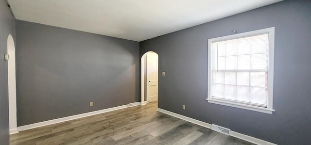 unfurnished room with baseboards, arched walkways, visible vents, and wood finished floors