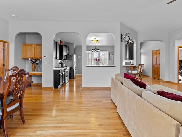 living room featuring baseboards, arched walkways, light wood finished floors, and a chandelier