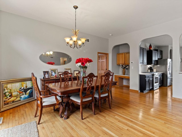 dining space featuring arched walkways, light wood-style floors, and a chandelier