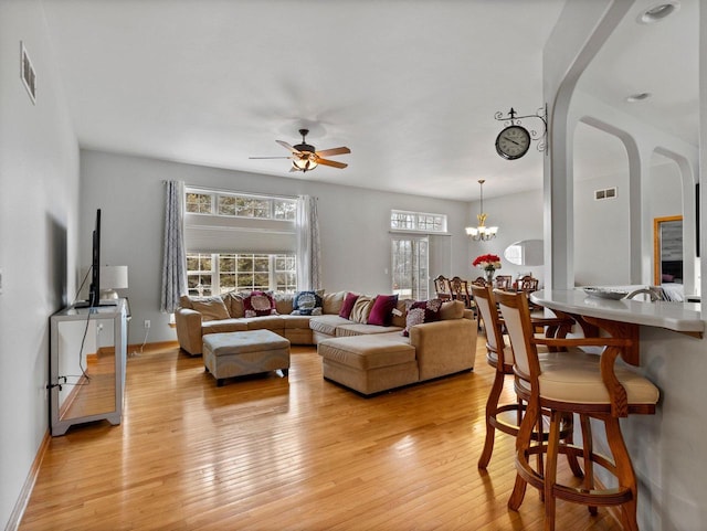 living area with light wood finished floors, visible vents, arched walkways, and ceiling fan with notable chandelier