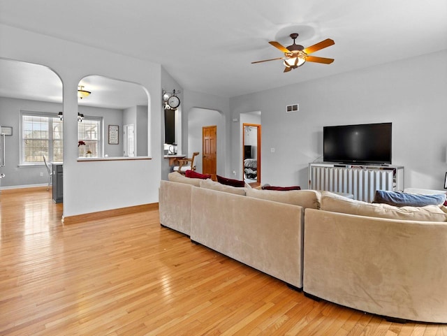 living room featuring visible vents, a ceiling fan, arched walkways, light wood-style floors, and baseboards