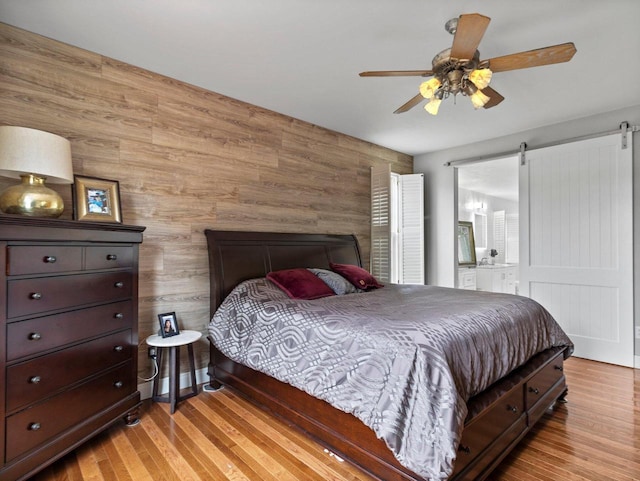 bedroom featuring ensuite bath, a barn door, wood finished floors, and ceiling fan