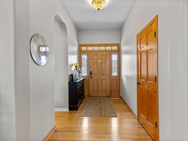 entryway featuring baseboards, arched walkways, and light wood-style flooring