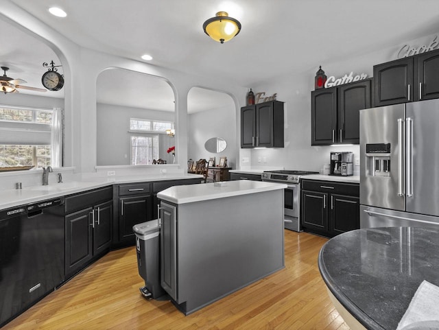 kitchen with arched walkways, a sink, appliances with stainless steel finishes, light wood-type flooring, and a center island