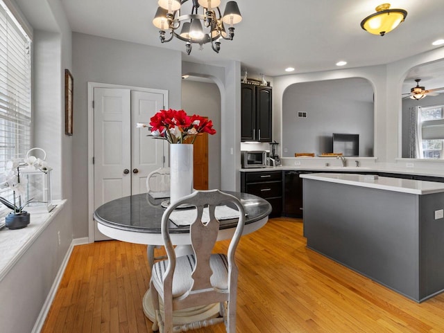 dining area featuring light wood finished floors, baseboards, recessed lighting, ceiling fan with notable chandelier, and arched walkways