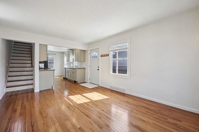 unfurnished living room with stairway, plenty of natural light, visible vents, and light wood-type flooring