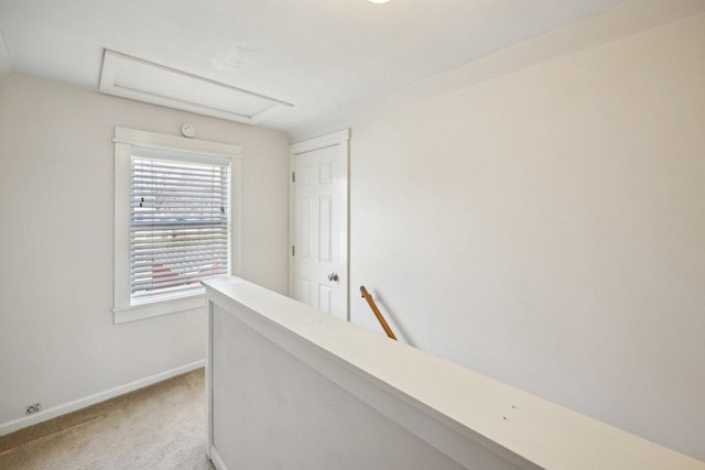 hallway featuring attic access, an upstairs landing, light colored carpet, and baseboards