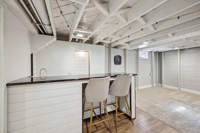 kitchen featuring dark countertops, a kitchen breakfast bar, wood finished floors, and a sink