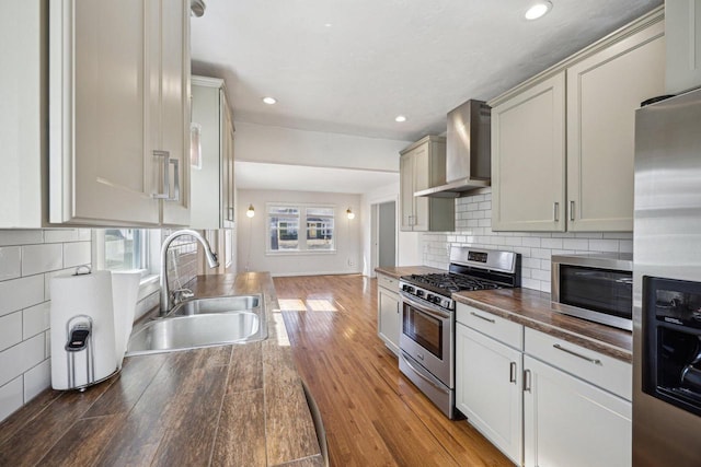 kitchen with a sink, decorative backsplash, stainless steel appliances, light wood-style floors, and wall chimney range hood