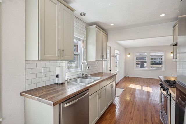 kitchen with baseboards, decorative backsplash, appliances with stainless steel finishes, hardwood / wood-style flooring, and a sink