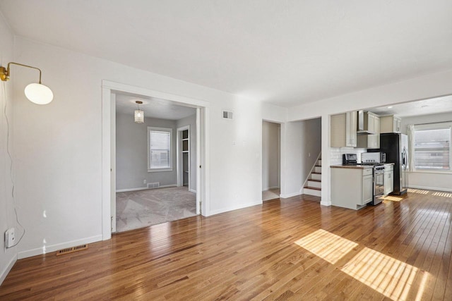 unfurnished living room with hardwood / wood-style floors, stairway, and visible vents