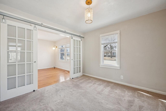 carpeted empty room featuring a barn door, plenty of natural light, and baseboards