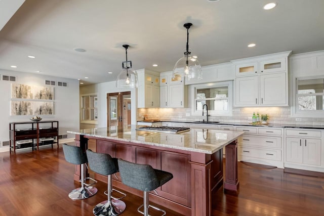 kitchen with light stone counters, visible vents, stainless steel gas cooktop, a sink, and decorative backsplash