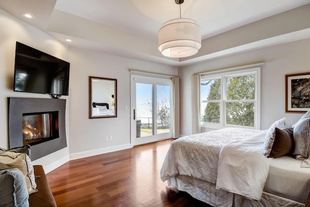 bedroom with access to outside, a glass covered fireplace, wood finished floors, recessed lighting, and baseboards