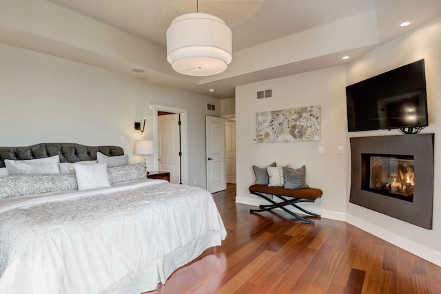 bedroom featuring wood finished floors, visible vents, baseboards, recessed lighting, and a glass covered fireplace