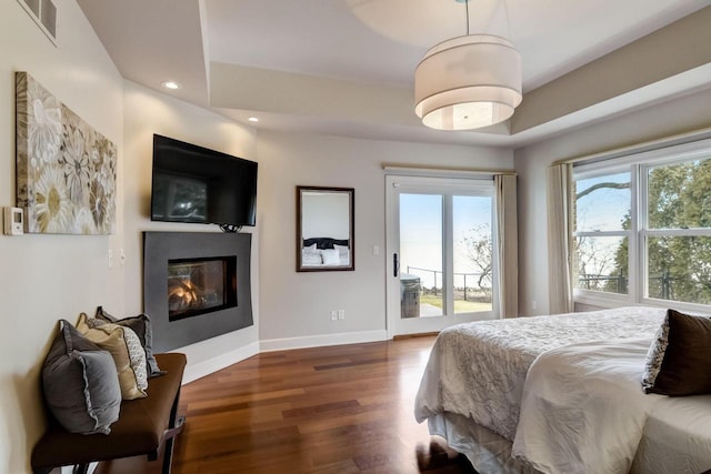 bedroom featuring access to exterior, multiple windows, baseboards, and wood finished floors