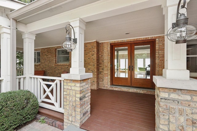 view of exterior entry featuring brick siding, a porch, and french doors