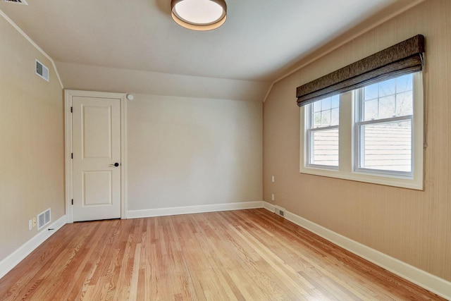 spare room featuring visible vents, baseboards, lofted ceiling, and light wood-style flooring