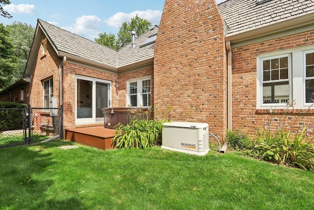 rear view of property with a yard, fence, brick siding, and a hot tub