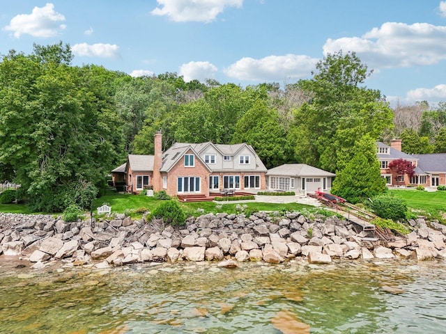 rear view of house with an outdoor structure, a chimney, a yard, and a water view