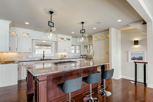 kitchen with stainless steel gas cooktop, a sink, a kitchen bar, backsplash, and a center island