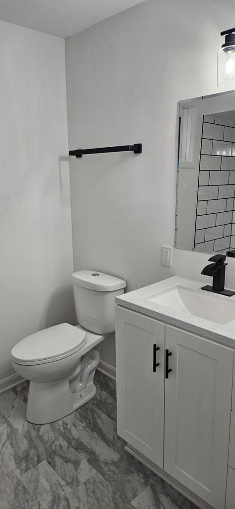 half bath with baseboards, toilet, marble finish floor, and vanity