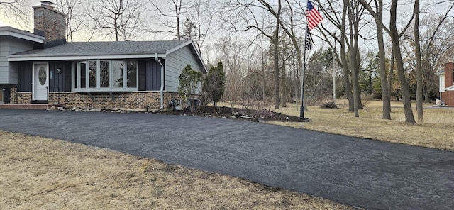 view of side of property with driveway, a chimney, and a yard