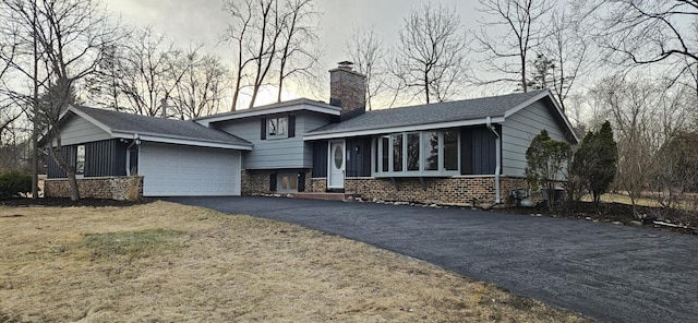 tri-level home with aphalt driveway, an attached garage, brick siding, and a chimney