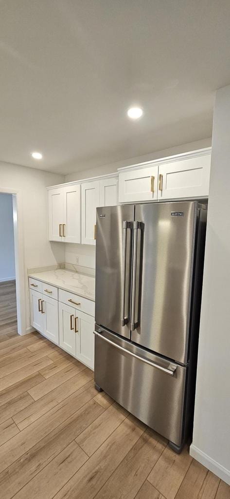 kitchen with light wood finished floors, high end fridge, white cabinets, and light stone countertops